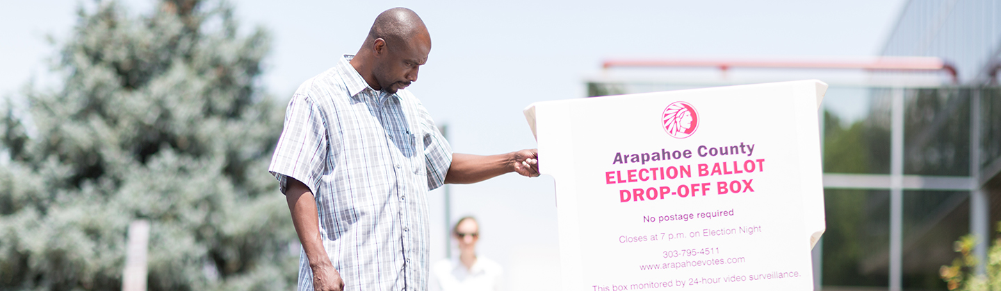 Man inserts ballot into white ballot box outdoors