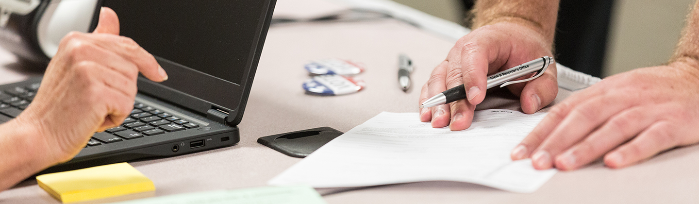 A pair of hands hold a pen and piece of paper on a table