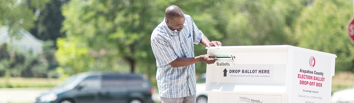 Man inserts ballot into white ballot box outdoors