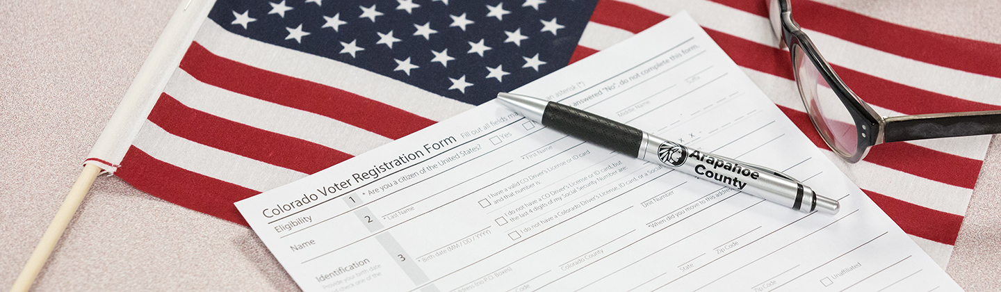 Pen and eyeglasses atop Colorado Voter Registration Form and small American flag