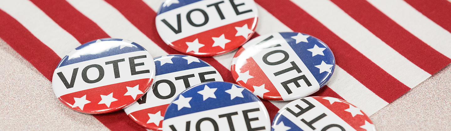 Six VOTE pins on top of an American flag