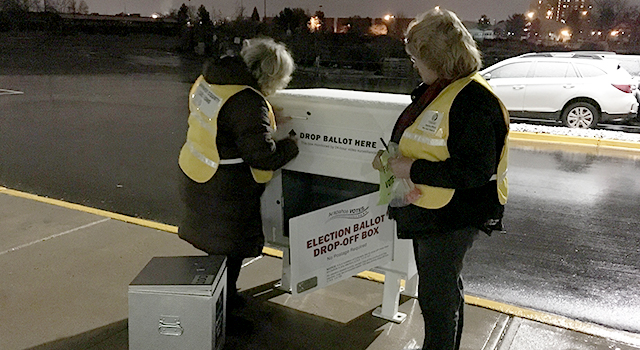 Two female election workers remove ballots from an outdoor ballot box at night