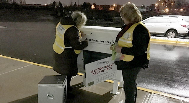 Two female election workers remove ballots from an outdoor ballot box at night
