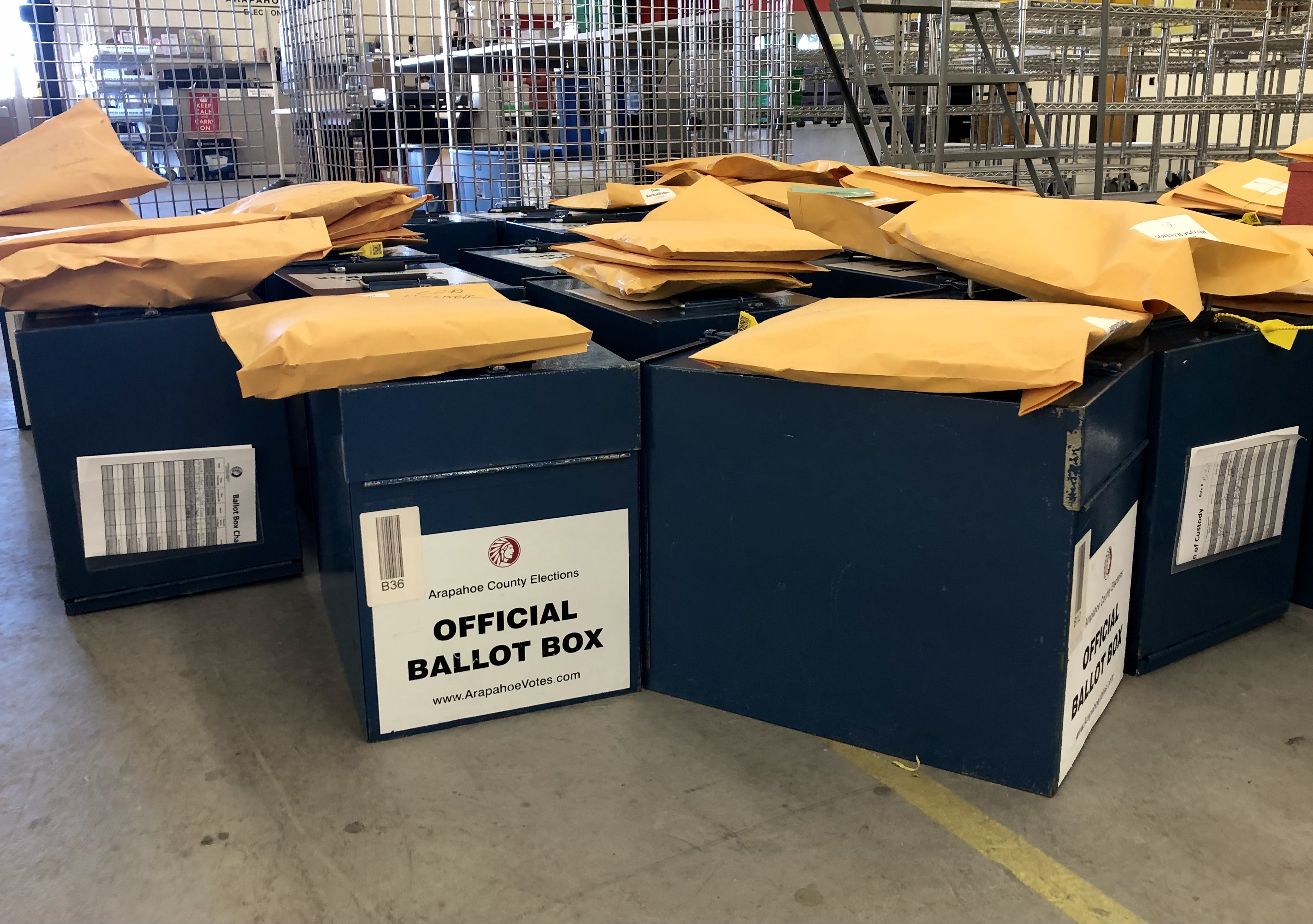 Ballot boxes sit on the floor with manila envelopes on top of them