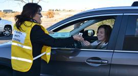 Female election worker in yellow vest gives sticker to female voter in car