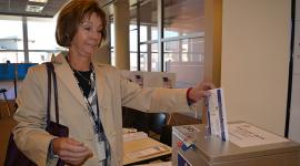 Female voter inserts ballot into ballot box on table in a room with windows