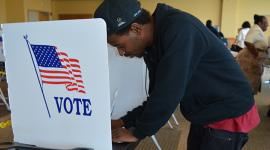 Male voter stands at voting booth and uses pen to mark his ballot