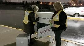 Two female election workers remove ballots from an outdoor ballot box at night