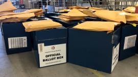 Ballot boxes sit on the floor with manila envelopes on top of them