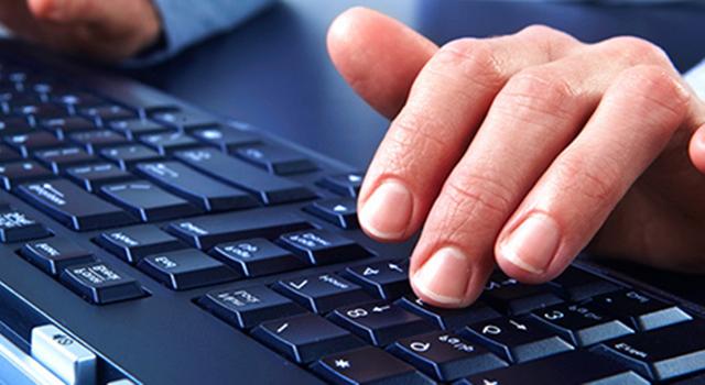 Fingers type on a white keyboard sitting on a black desk