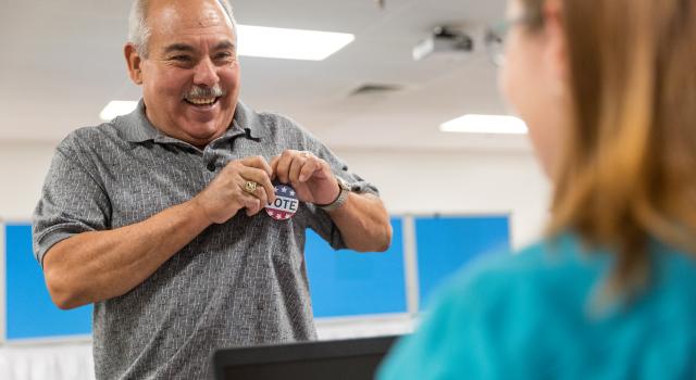 Man smiling puts I Voted button onto shirt