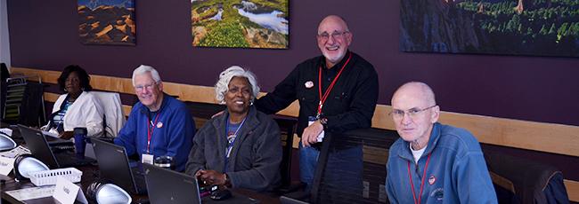 Five election judges sit at laptops at a table in a Voter Service and Polling Center.